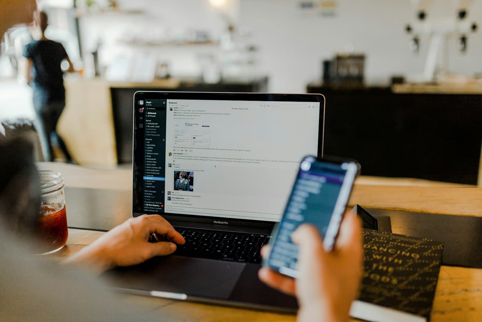 A person checking a phone while working on a laptop
